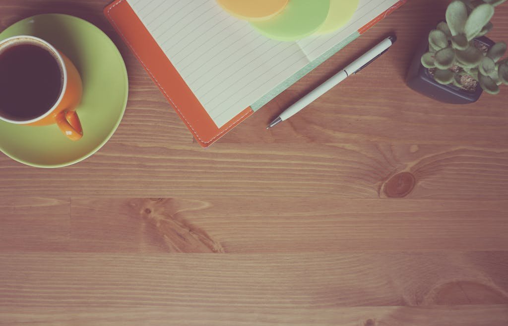 A warm-toned workspace with a cup of coffee, notebook, pen, and succulent on a wooden table.